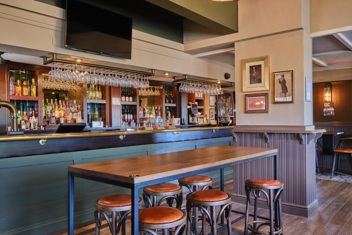 Cosy pub bar with hanging glassware and leather stools
